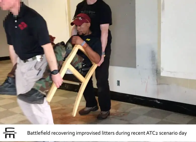 Two handsome and burly men lift a simulated casualty in a standard office chair