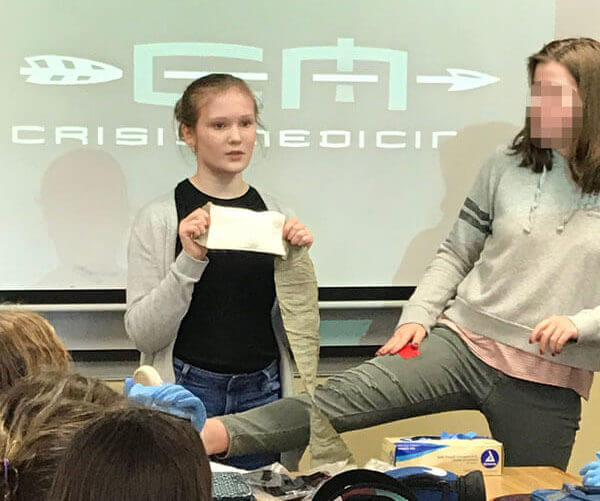 a girl holds up a bandage in preparation to put it on a simulated wound on her friend's leg