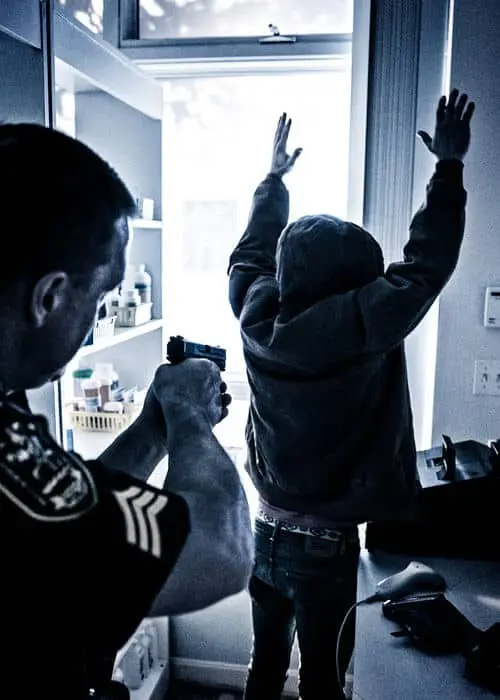 A suspect held at gunpoint by police after stealing prescriptions from a pharmacy. The police have their guns drawn on the suspect while the subject has his arms in the air.