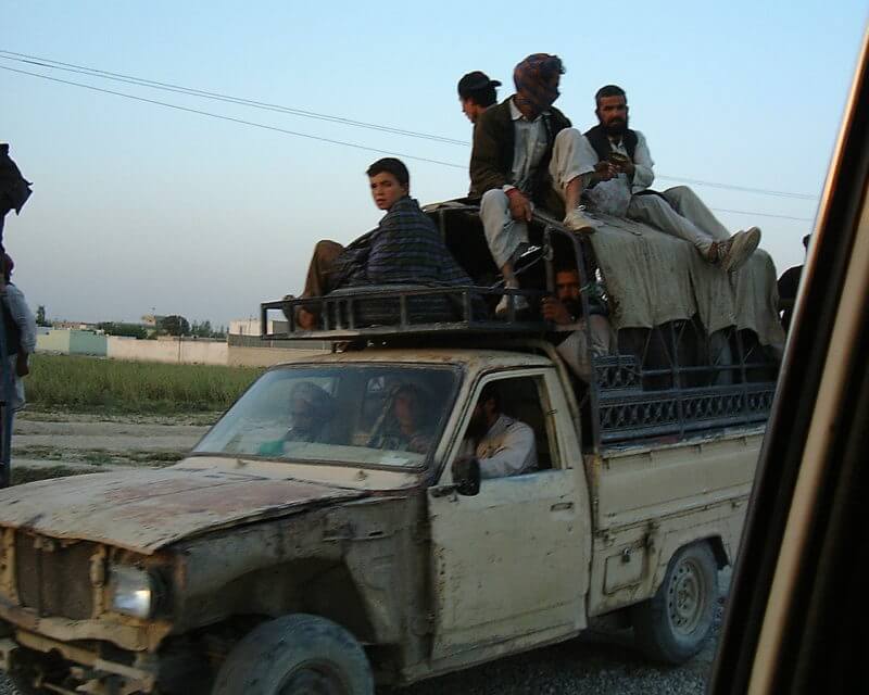 men riding on a roof rack over a pickup truck in Afghanistan