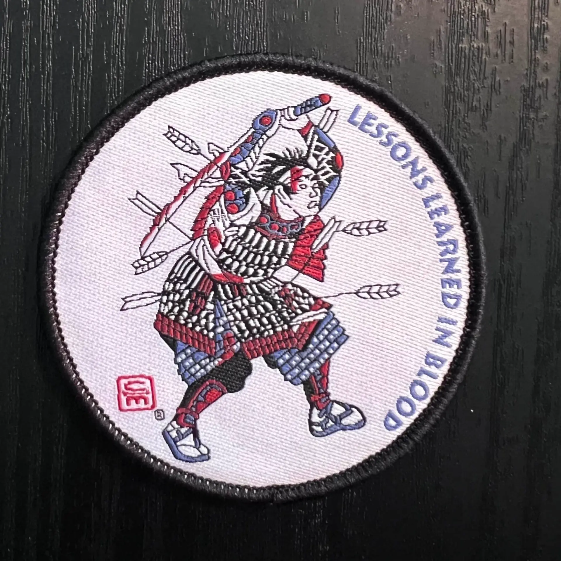 Samurai 3in Patch A woven patch with marrow edge and velcro backing showing a Samurai in battle, bloodied and shot full of arrows, with a broken and bloodied sword raised overhead