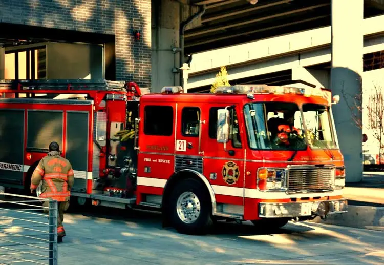 A firghfigher walks over to a firetruck parked in front of a high rise structure