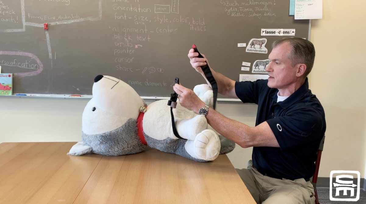 Dr. Shertz shows proper application of a tourniquet on a giant stuffed dog while sitting in an elementary school desk