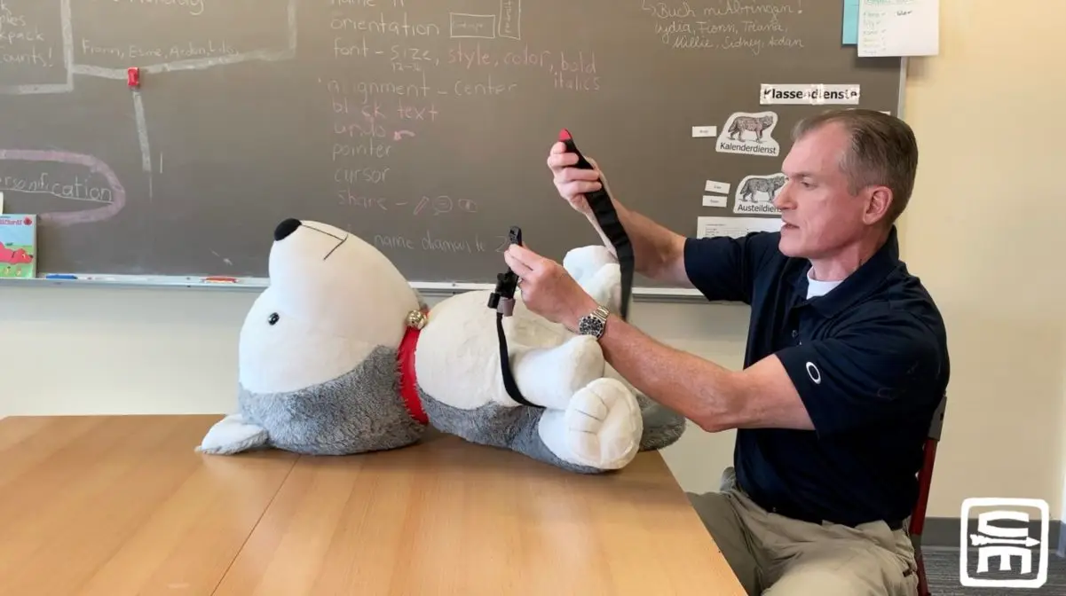 Dr. Shertz shows proper application of a tourniquet on a giant stuffed dog while sitting in an elementary school desk