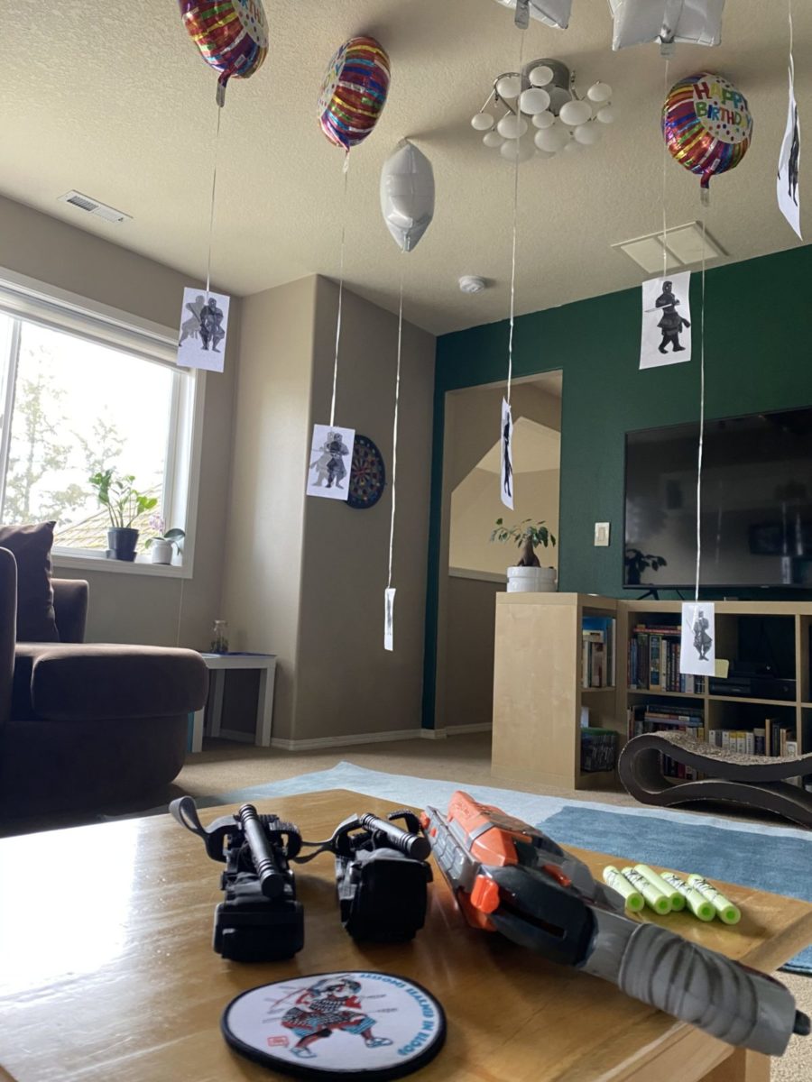 A photo showing a residential room with helium balloons holding aloft paper ninja targets with a nerf gun, nerf ammunitions, two tourniquets, and a crisis medicine patch in the foreground