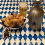 A perfect Oktoberfest display with homemade pretzels, a perfectly poured beer, and a new Crisis Medicine custom Growler on a traditional blue and white checked table
