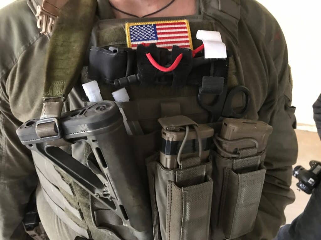 A photo of the burly chest of an operator with an American flag and CAT tourniquet staged on the exterior of his gear, center line