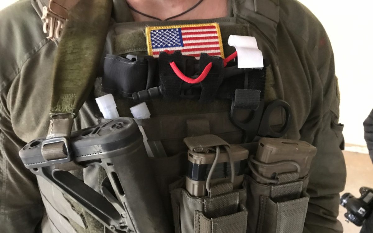 A photo of the burly chest of an operator with an American flag and CAT tourniquet staged on the exterior of his gear, center line