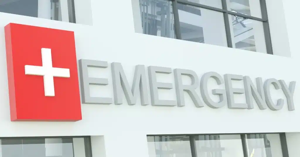 A sign on what is clearly a hospital that says EMERGENCY with a white cross in a red square