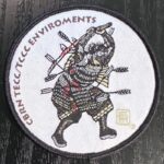 A woven patch with marrow edge and velcrow backing showing a Samurai in battle, bloodied and shot full of arrows, wearing a gas mask