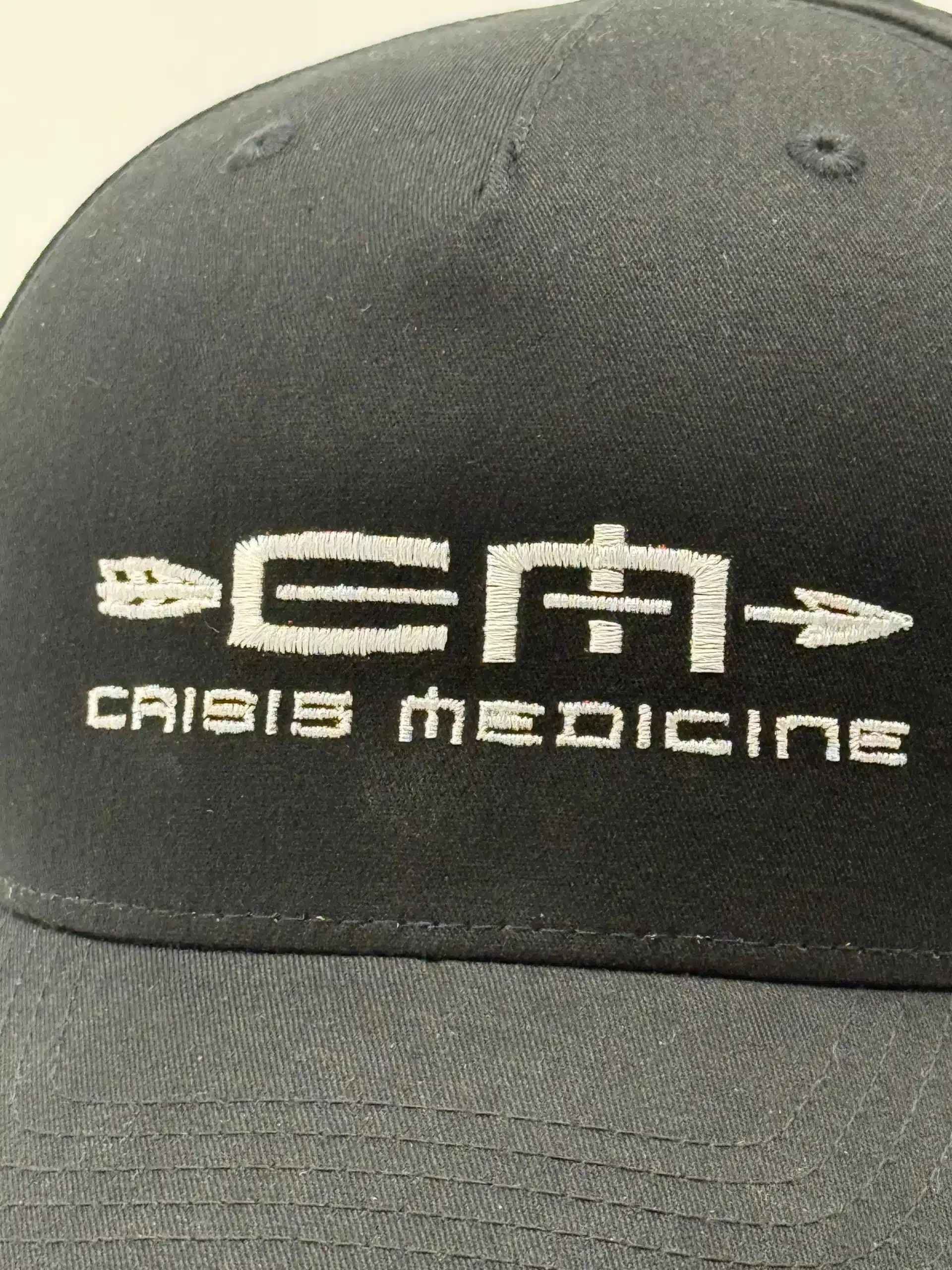 Closeup of the brim of the Crisis Medicine logo'd baseball hat